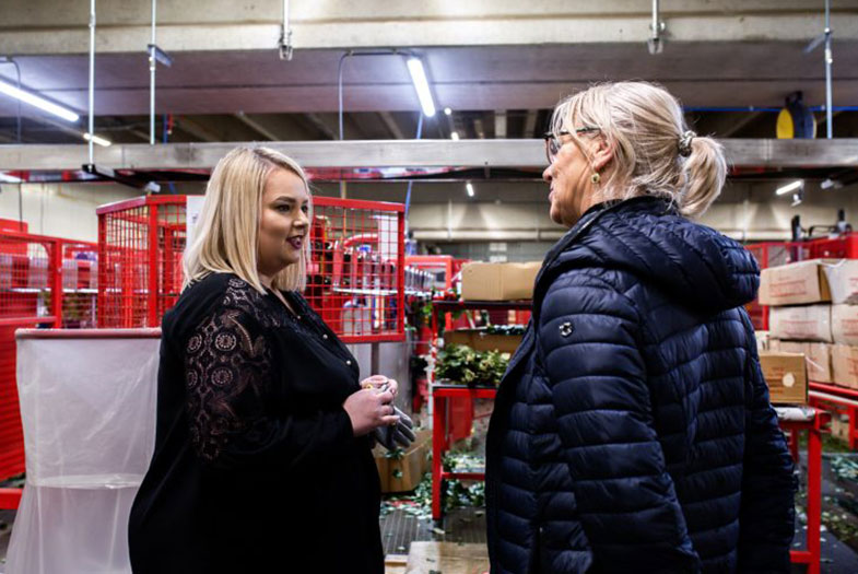 Twee vrouwelijke medewerkers in gesprek in een agrarisch magazijn tussen rode kratten.